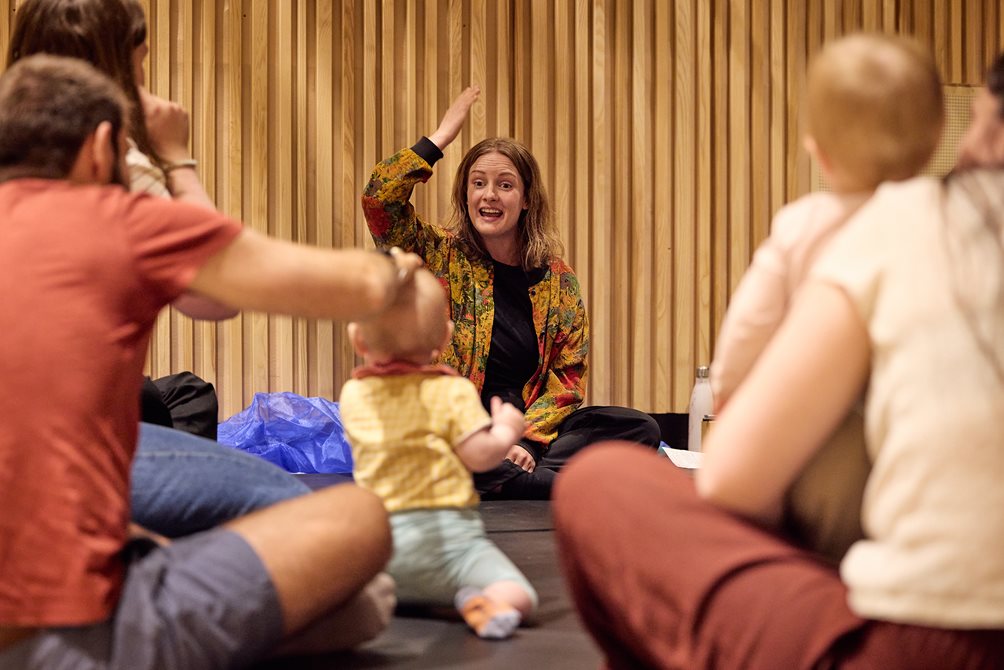 Kathrine Tendal løfter en arm opp mens hun ser mot en gruppe små barn